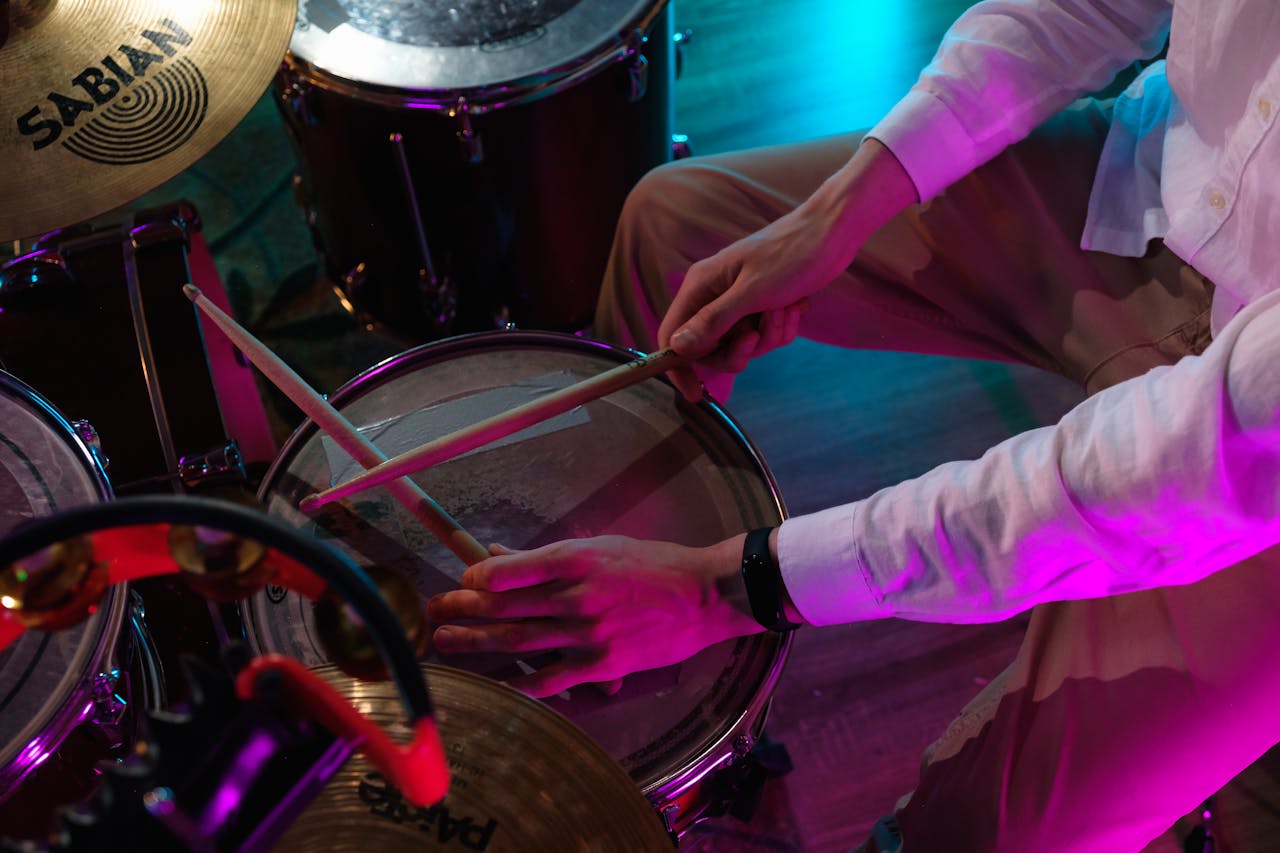 Close-up of drummer playing in a vibrant music studio setting with colorful lighting.